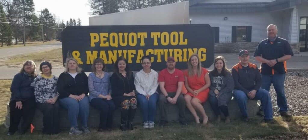 Pequot Tool staff standing and sitting in front of the Pequot Tool sign