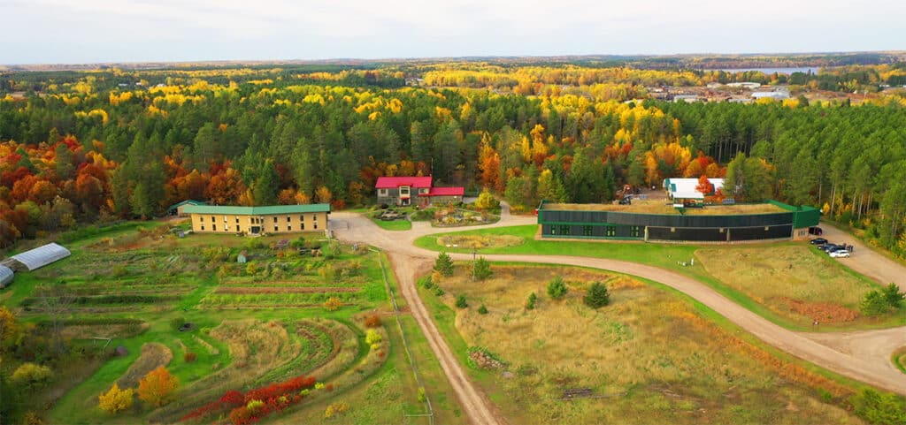 Aerial Photo of Hunt Utilities Group showing several buildings with large gardens and lawn surounding them along the edge of a forest of pine trees in the background on a warm fall day