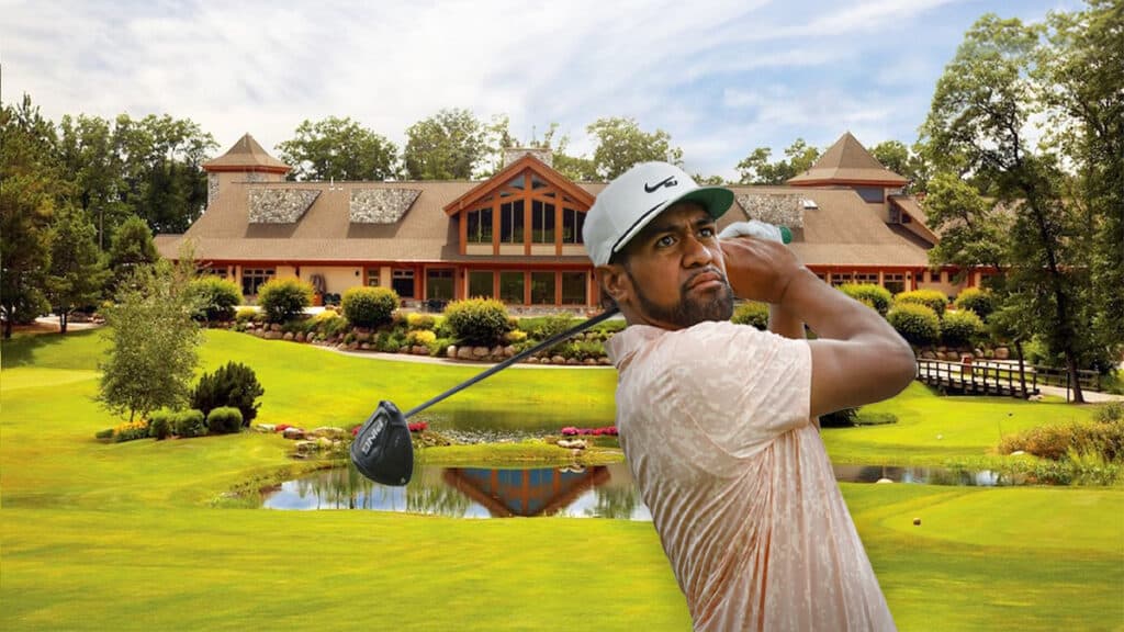 Image of a man swinging a golf club at a golf course with the clubhouse in the background on a summer day