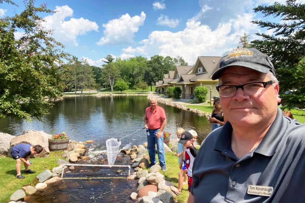 Photo of a middle aged man at Kavanaugh's Sylvan Lake Resort with another man and children in the background playing by a pond