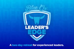 Blue gradient background with the words Leaders Edge repeated in the background with a crest-like logo on top in blue and white that says Leader's Edge