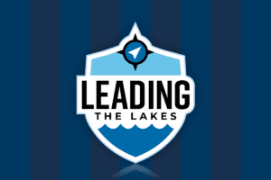 Blue, navy blue, white and black logo for Leading the lakes with a dark blue and darker navy blue striped background