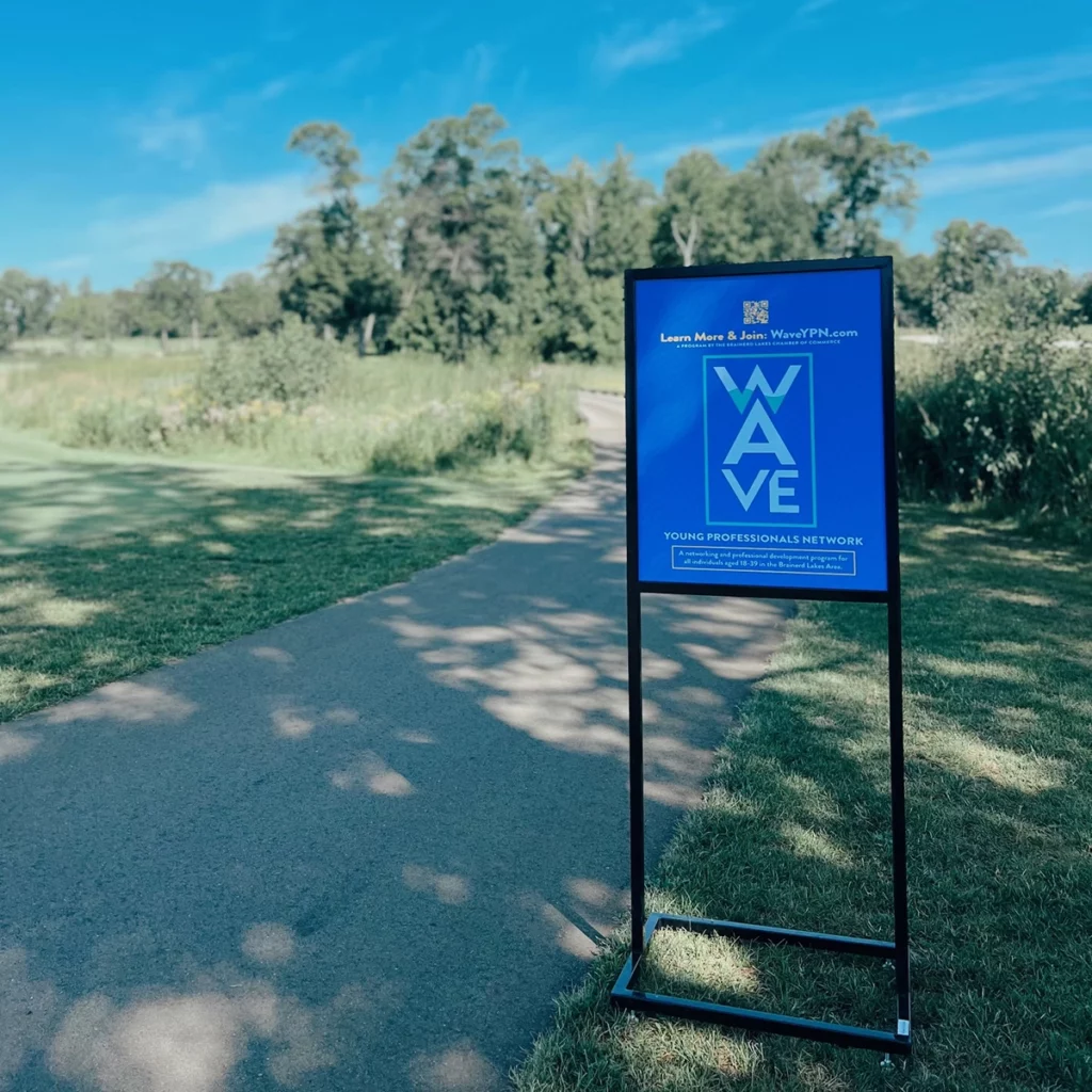 Photo of a large, blue sign with a golf course in the background on a sunny summer day