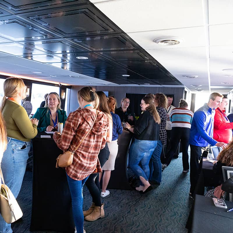 Photo from WAVE Young Professionals Launch Event showing a group of young adults networking and talking within a crowd of people on a cruise ship interrior square