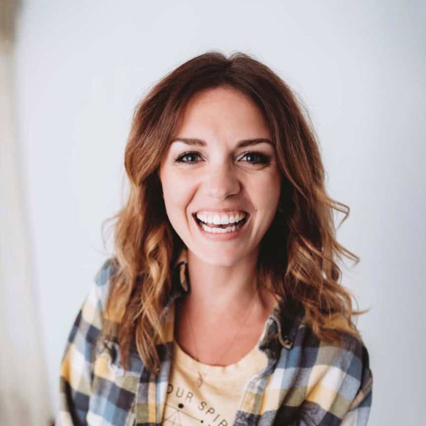 Headshot of a smiling, young woman with brown hair wearing a plaid orange shirt